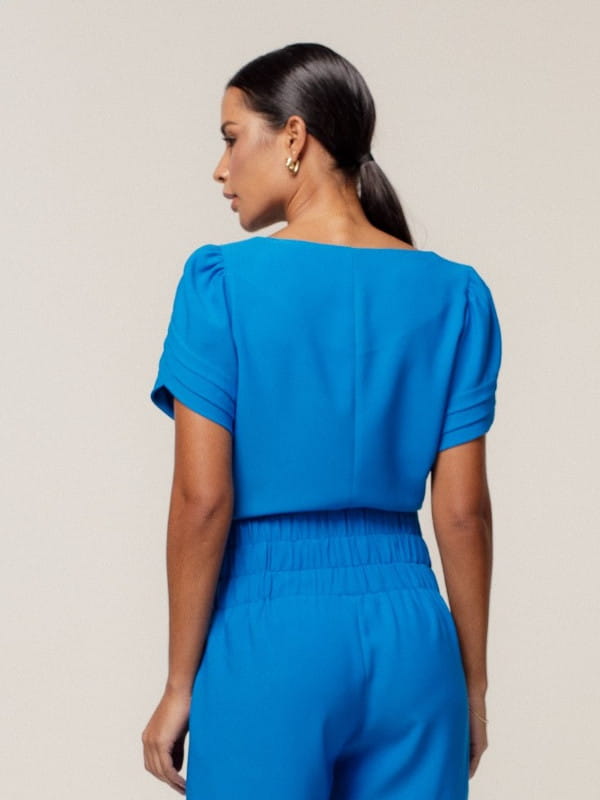 Blusas femininas delicadas: modelo vestindo uma blusa de crepe alfaiataria decote redondo azul - costas.
