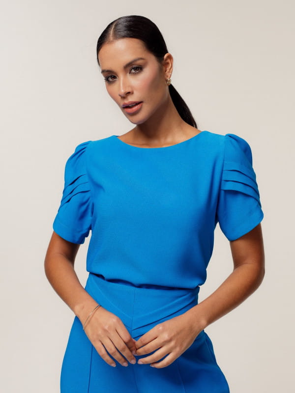 Blusas femininas delicadas: modelo vestindo uma blusa de crepe alfaiataria decote redondo azul.