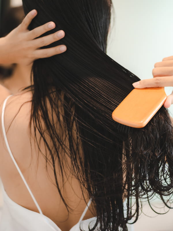 Como cuidar da beleza no verão: mulher cuidando escovando os cabelos hidratados.