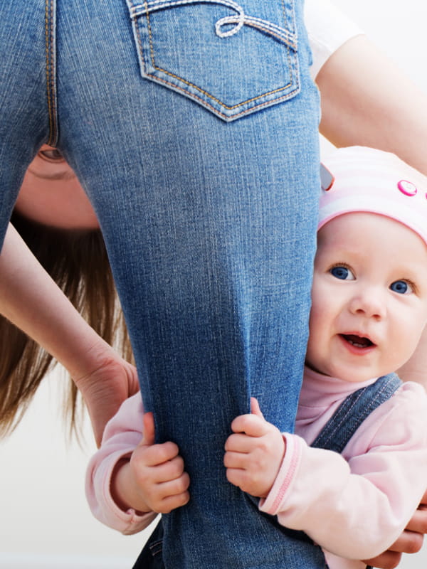 Como usar calça jeans: filha segurando na perna da mãe que está usando uma calça jeans.